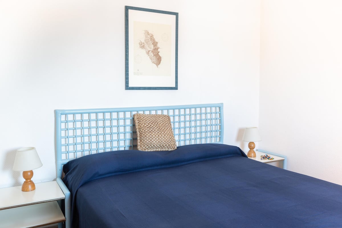 Un lit bien fait, avec une tête de lit bleue et une carte encadrée accrochée au mur.