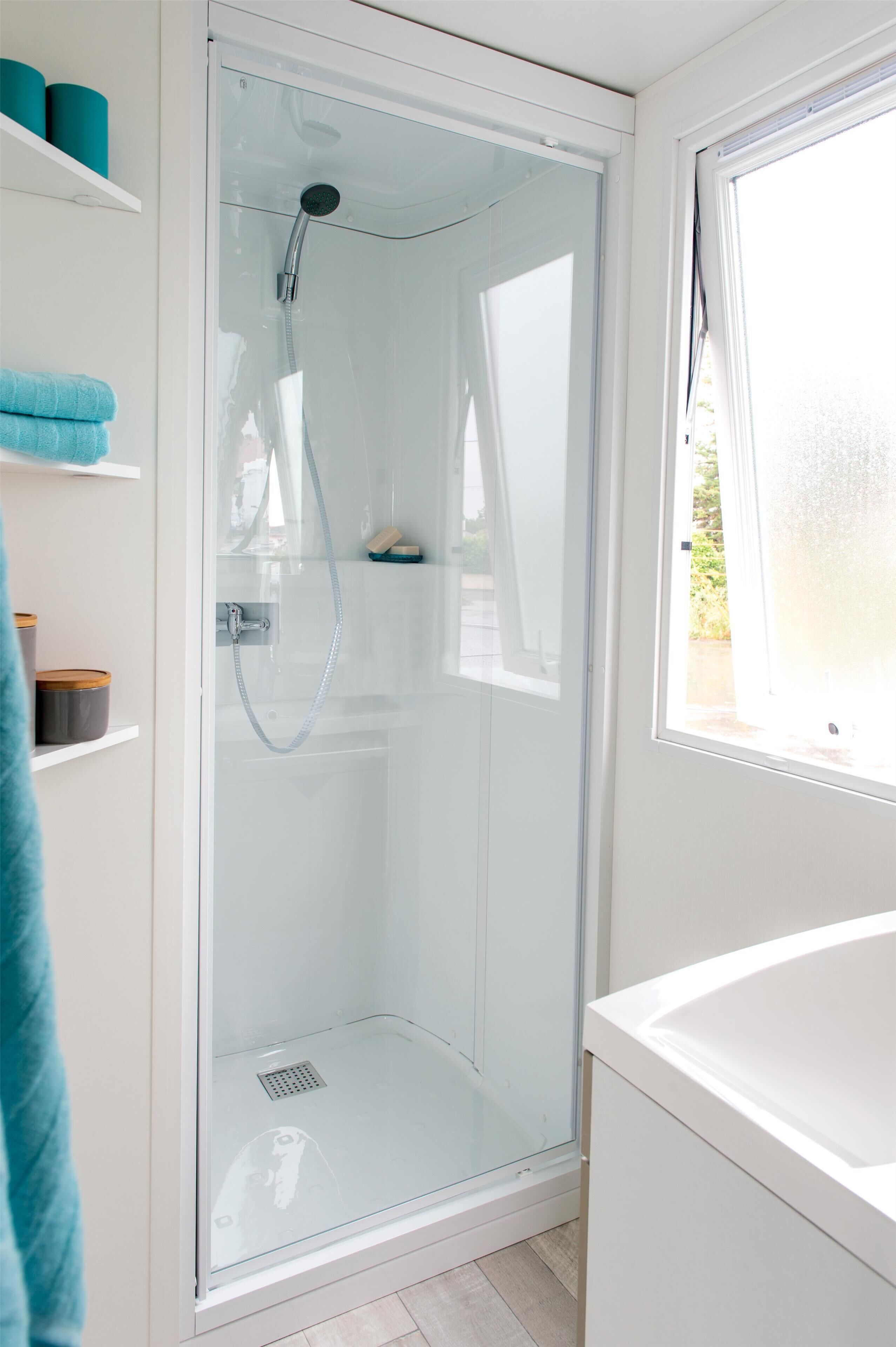 A modern bathroom with a glass-enclosed shower, a white sink, and a window providing natural light.