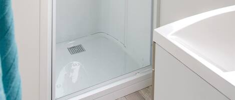 A modern bathroom with a glass-enclosed shower, a white sink, and a window providing natural light.