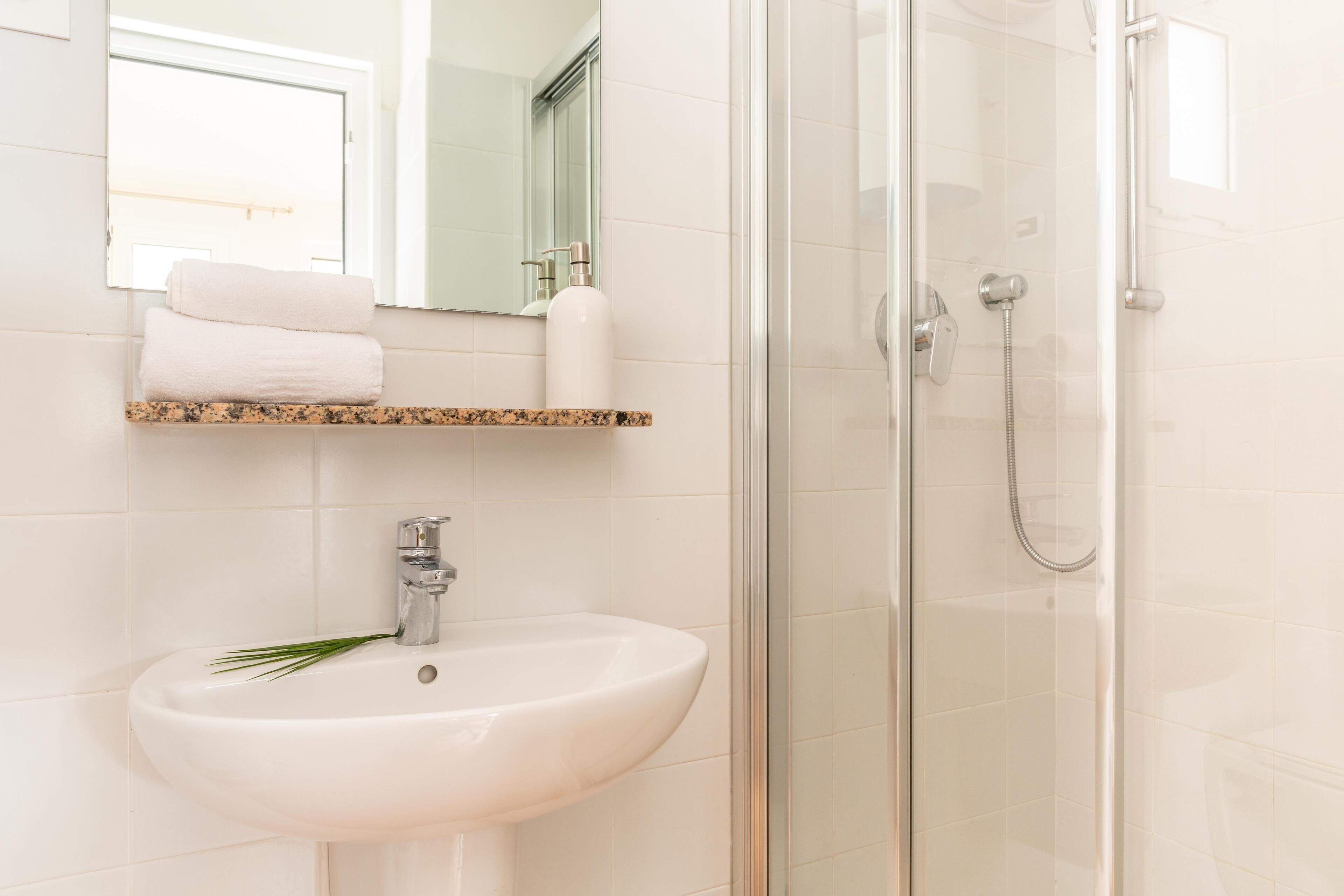 Un baño con un lavabo blanco, cabina de ducha con mampara de vidrio y un espejo sobre el lavabo.