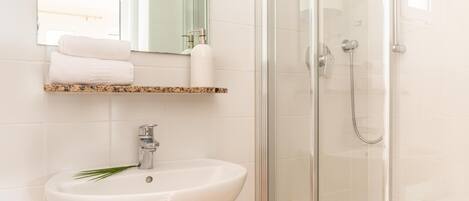 Un baño con un lavabo blanco, cabina de ducha con mampara de vidrio y un espejo sobre el lavabo.