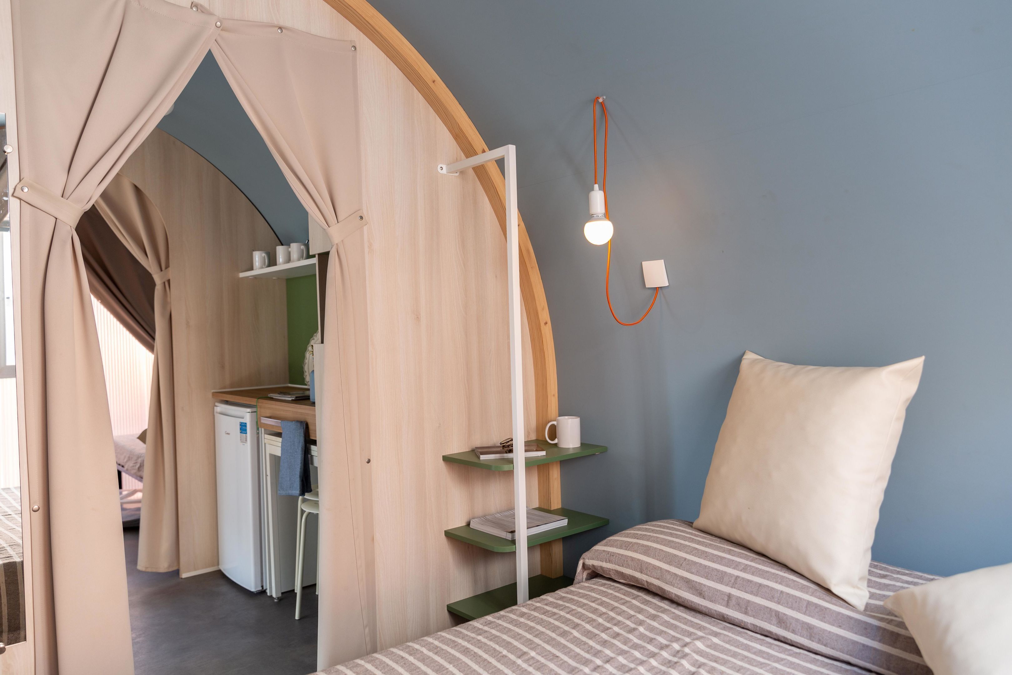 Een kamer met een bed, een bureau, een stoel, een kleine koelkast en een lamp.