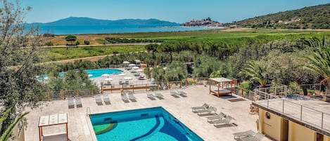 A pool with a geometric design, sun loungers, and a view of the sea and hills.