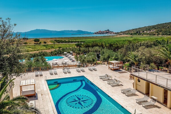 Una piscina con diseño geométrico, tumbonas y vistas al mar y a las colinas.
