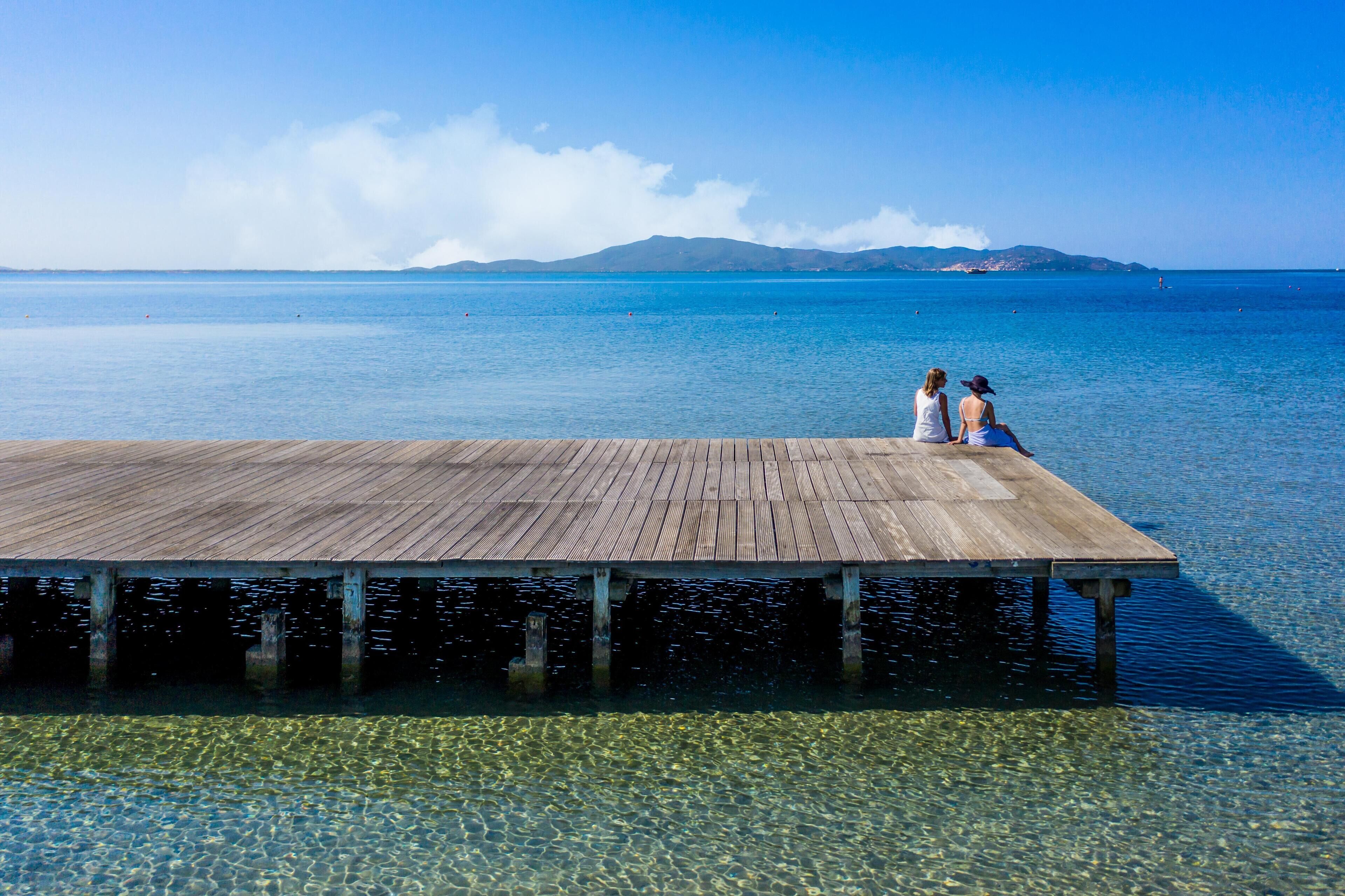 Une jetée en bois s’étendant sur une étendue d’eau calme et limpide, avec une chaîne de montagnes visible au loin.