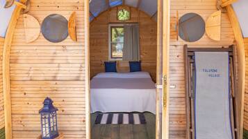 Una cabaña de madera con una cama, una ventana, una puerta y un farol.