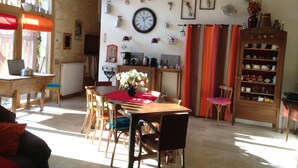 A rustic dining area with a wooden table, chairs, and a vase of flowers. A clock and various kitchen utensils are mounted on the wall. - Domaine de la Haute Poignandière (Saint-Germain-de-la-Coudre)