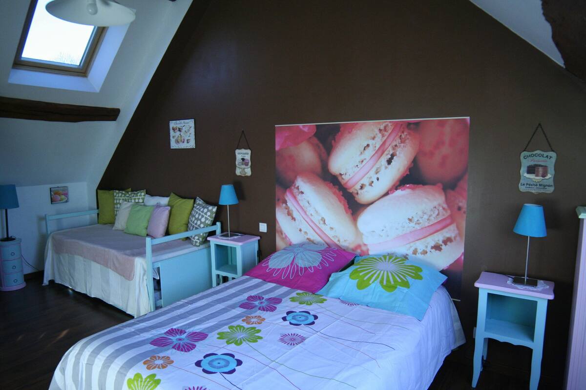 Une chambre avec un plafond en pente, un grand lit avec une literie à motifs floraux, deux tables de chevet avec des lampes et une affiche accrochée au mur.