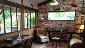 A cozy room with a brick wall, a large window, a leather armchair, a small table, and a patterned rug. - Domaine de la Haute Poignandière (Saint-Germain-de-la-Coudre)