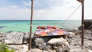 Boscam aeri de fusta amb trulls de colors penjats, davant d'una platja rocosa i un mar turquesa.