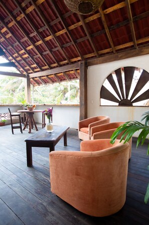 An outdoor seating area with wooden furniture, a round table, and a decorative wall piece. - The Safe House (Tulum)
