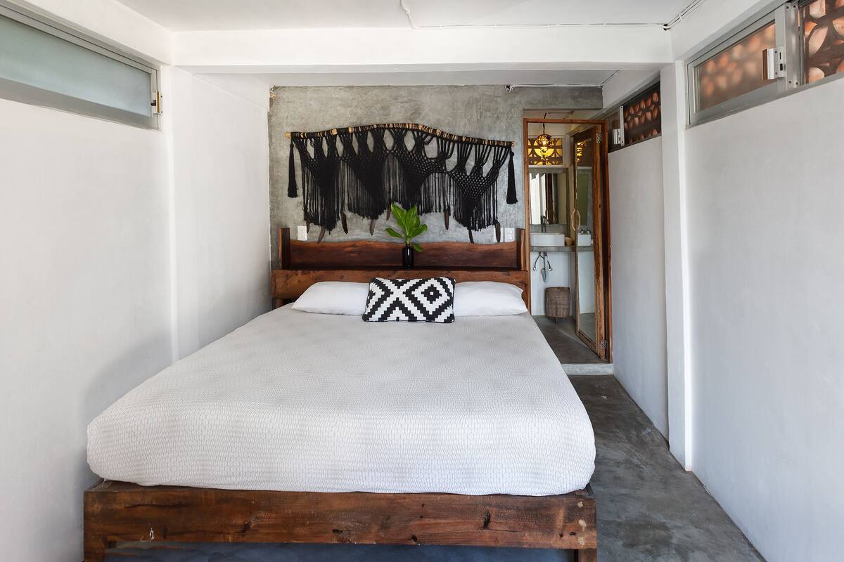 A bed with a white textured bedspread, a wooden headboard, and a macramé wall hanging above it.
