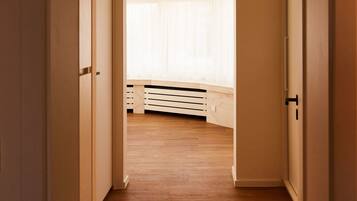 A hallway with wooden flooring leading to a room with a large window and a bed.