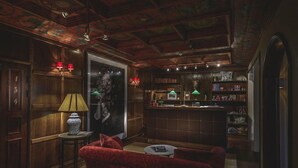 A room with a red sofa, a small table, a lamp, a bookshelf, and a bar area.