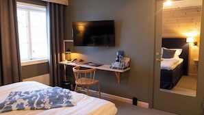 A hotel room with a bed, a desk with a chair, a television, and a mirror.