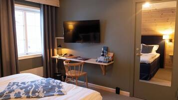 Ett hotellrum med en säng, ett skrivbord med en stol, en tv och en spegel.