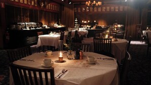 A dimly lit restaurant with round tables, chairs, and a bar area in the background.