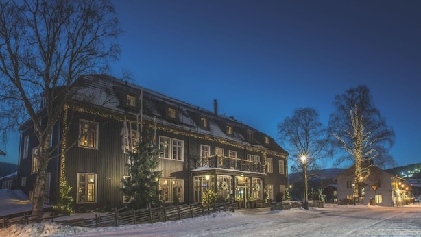 A large, multi-story building with a balcony, surrounded by snow, at twilight.