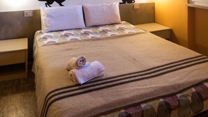 A neatly made bed with a patterned bedspread, two pillows, and a folded towel. There are two wall-mounted nightstands with a cat silhouette decoration on each. - Colors Hostel (Toscolano Maderno)
