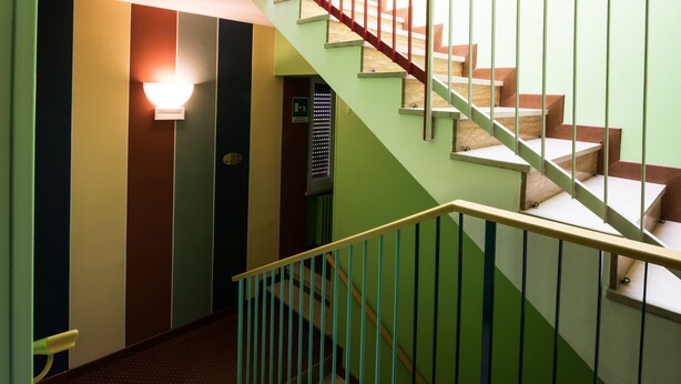 A staircase with a green handrail and wooden steps, leading to an elevator. - Colors Hostel (Toscolano Maderno)