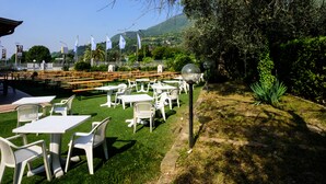 An outdoor seating area with tables and chairs, a lamp post, and a view of a mountainous landscape. - Colors Hostel (Toscolano Maderno)