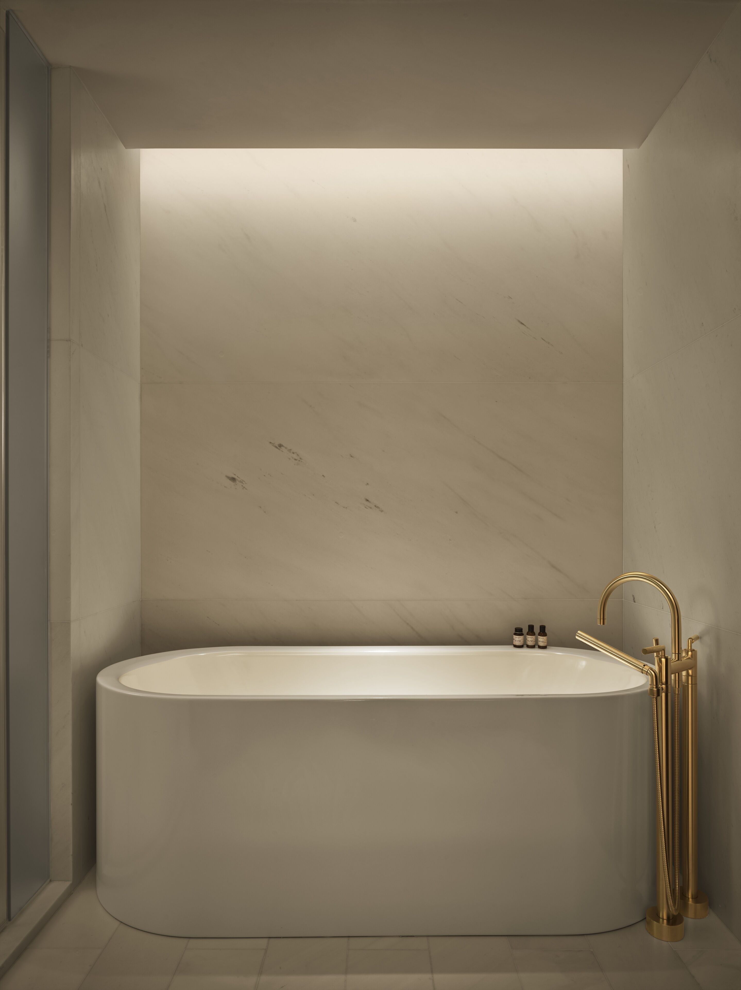 Een moderne badkamer met een vrijstaand bad, een gouden kraan en een wandlamp.