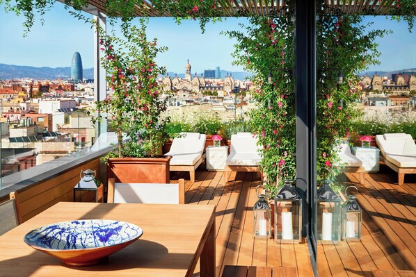 A rooftop terrace with wooden flooring, lounge chairs, a table with a bowl, and potted plants. - The Barcelona EDITION (Barcelona)