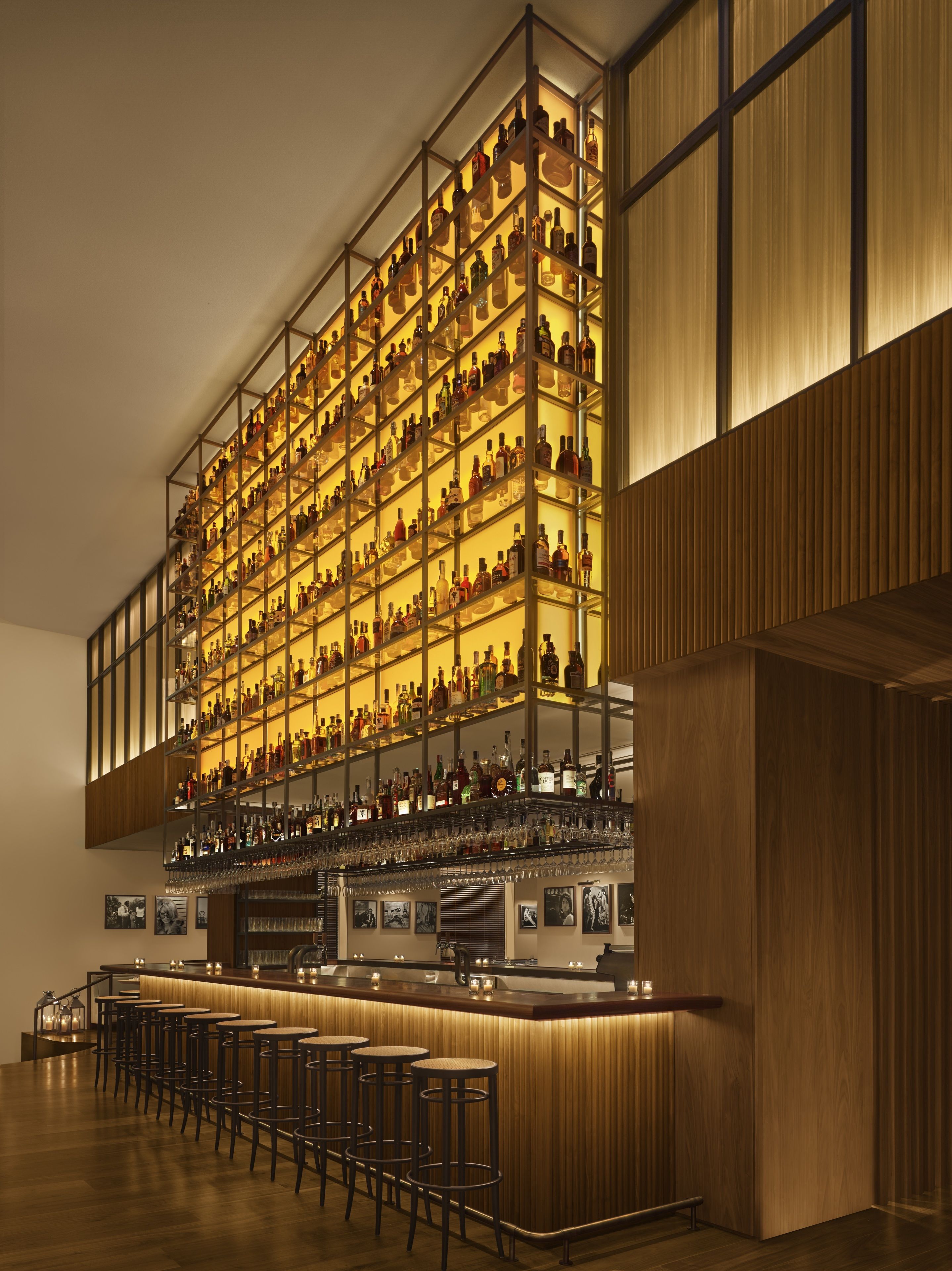 A bar area with multiple shelves of bottles and glasses, wooden bar counter, and bar stools.