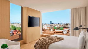 Una habitación de hotel moderna con una cama grande, un televisor de pantalla plana y un balcón con vistas a la ciudad.