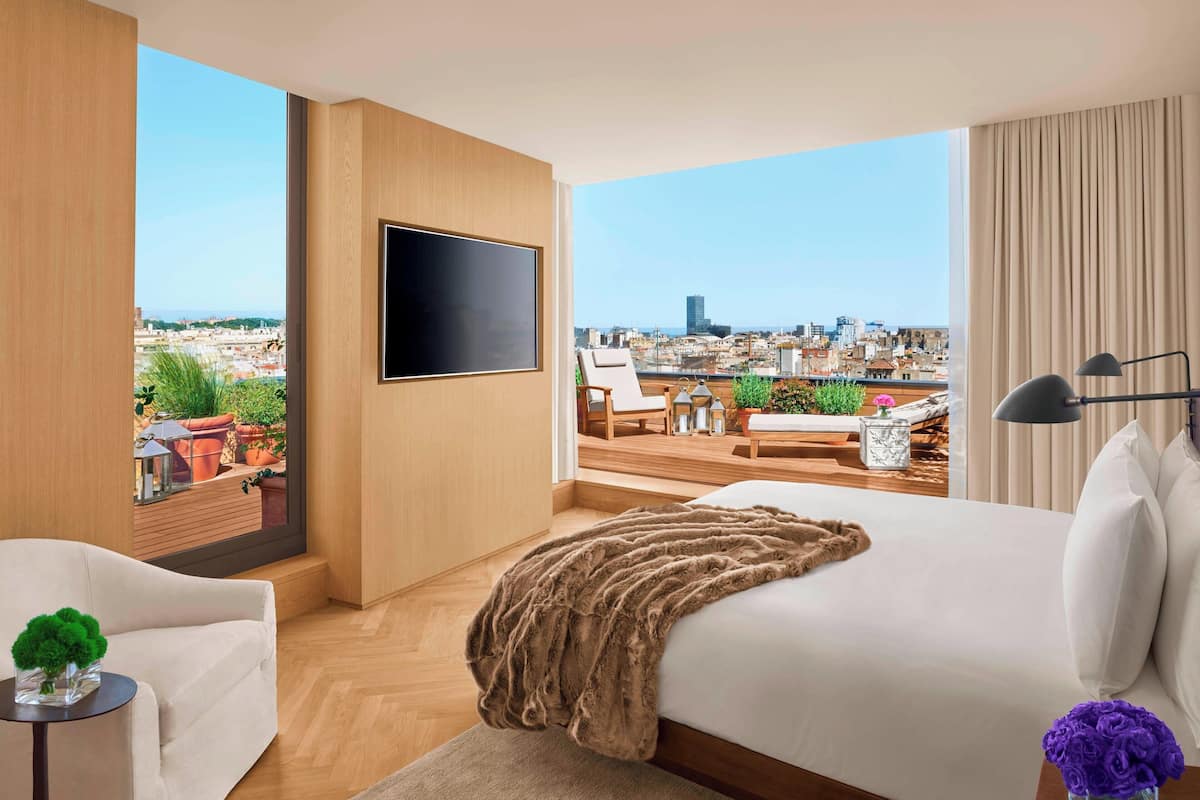 Moderni hotellihuone, jossa on suuri sänky, taulutelevisio ja parveke, jolta on näkymä kaupunkiin.