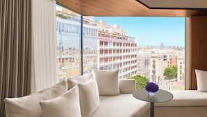 Una sala de estar moderna con un gran ventanal que ofrece vistas a la ciudad, un sofá blanco y una mesita redonda con un florero.
