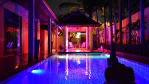 Piscina con suelo de baldosas y zona de estar techada con sillas.