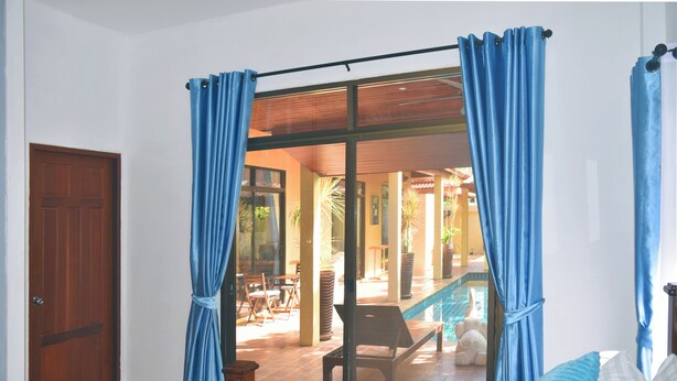Un dormitorio con una cama grande, vista a un área de piscina al aire libre y cortinas azules.