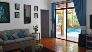 Un salón con sofá, una mesa de centro y un mueble para televisión. Hay una puerta que da a un balcón con piscina.