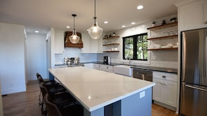 A modern kitchen with a large island, pendant lighting, and built-in shelving.