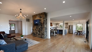 A spacious living area with a stone accent wall, a flat-screen TV, and a modern kitchen in the background.
