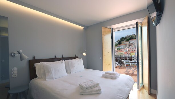 Ein modernes Schlafzimmer mit einem großen Bett, einem hölzernen Kopfteil und Blick auf eine Stadtlandschaft durch eine geöffnete Tür.