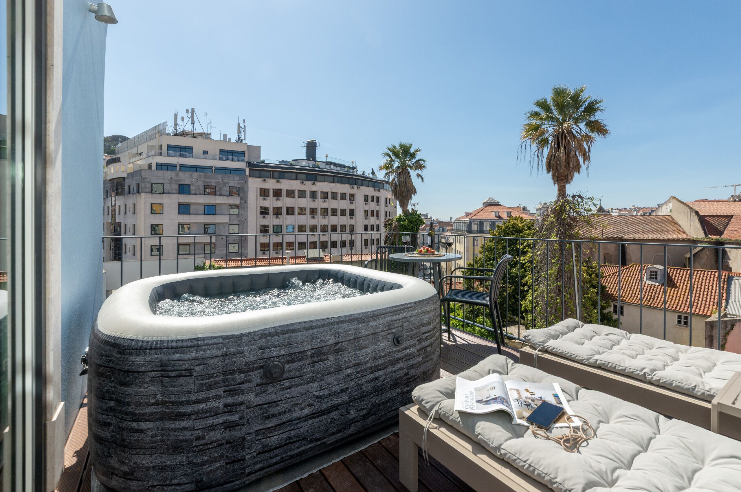 Un jacuzzi en un balcón con vista a edificios y una palmera.