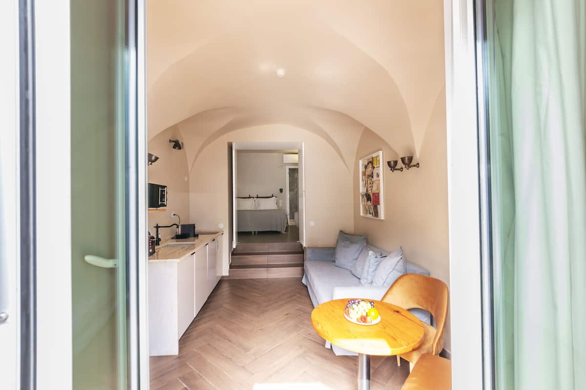 Un intérieur comprenant une cuisine, un coin repas et un espace de vie, avec un parquet disposé en chevrons et un plafond en arc de cercle.