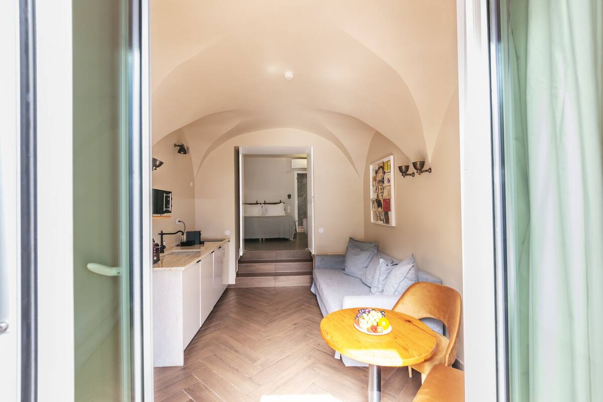 Un interior con cocina, comedor y sala de estar, destacando un suelo con patrón de espiga y un techo abovedado.