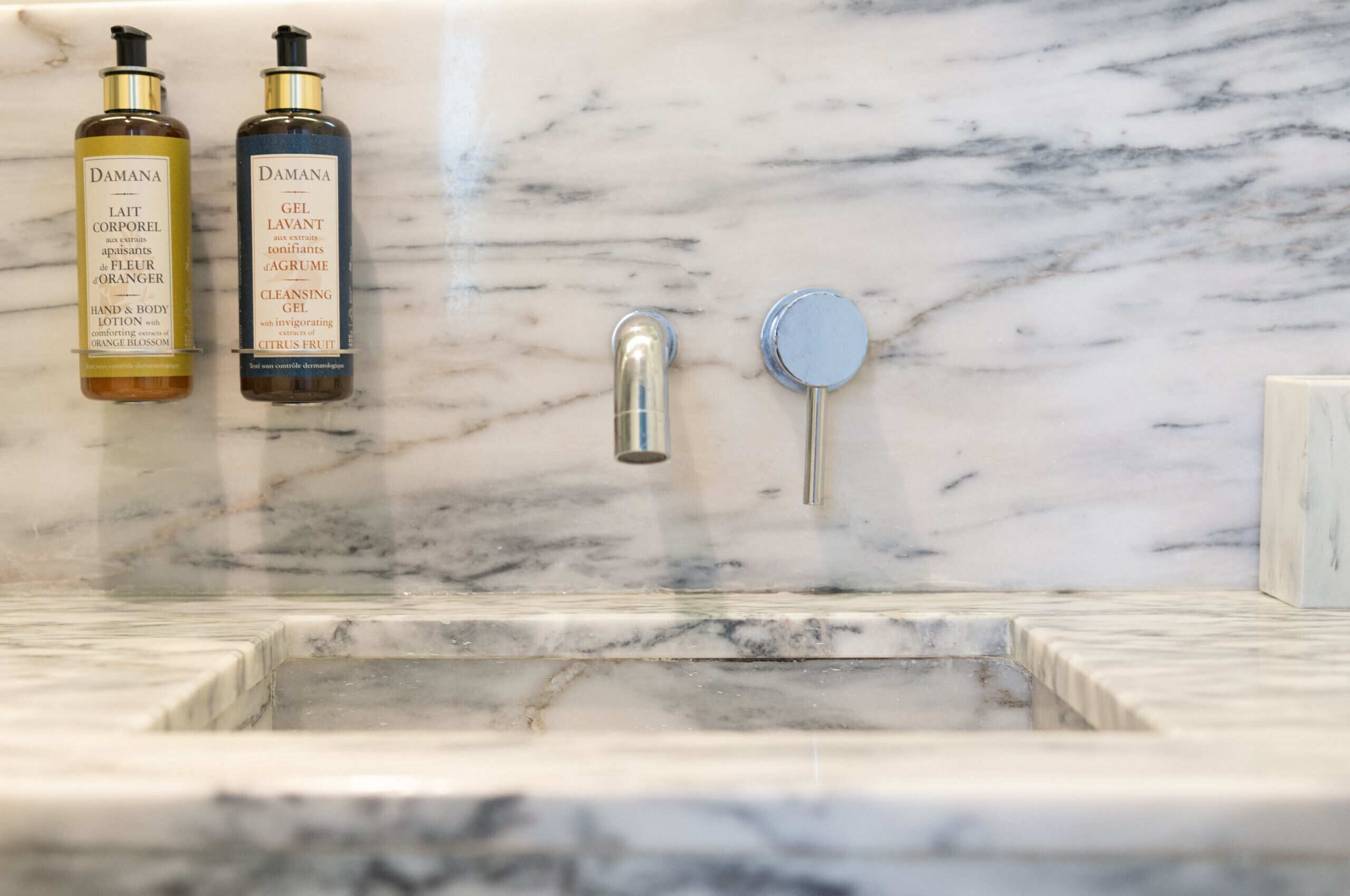 Un baño con encimera de mármol, un lavamanos y dos botellas de productos Damana.