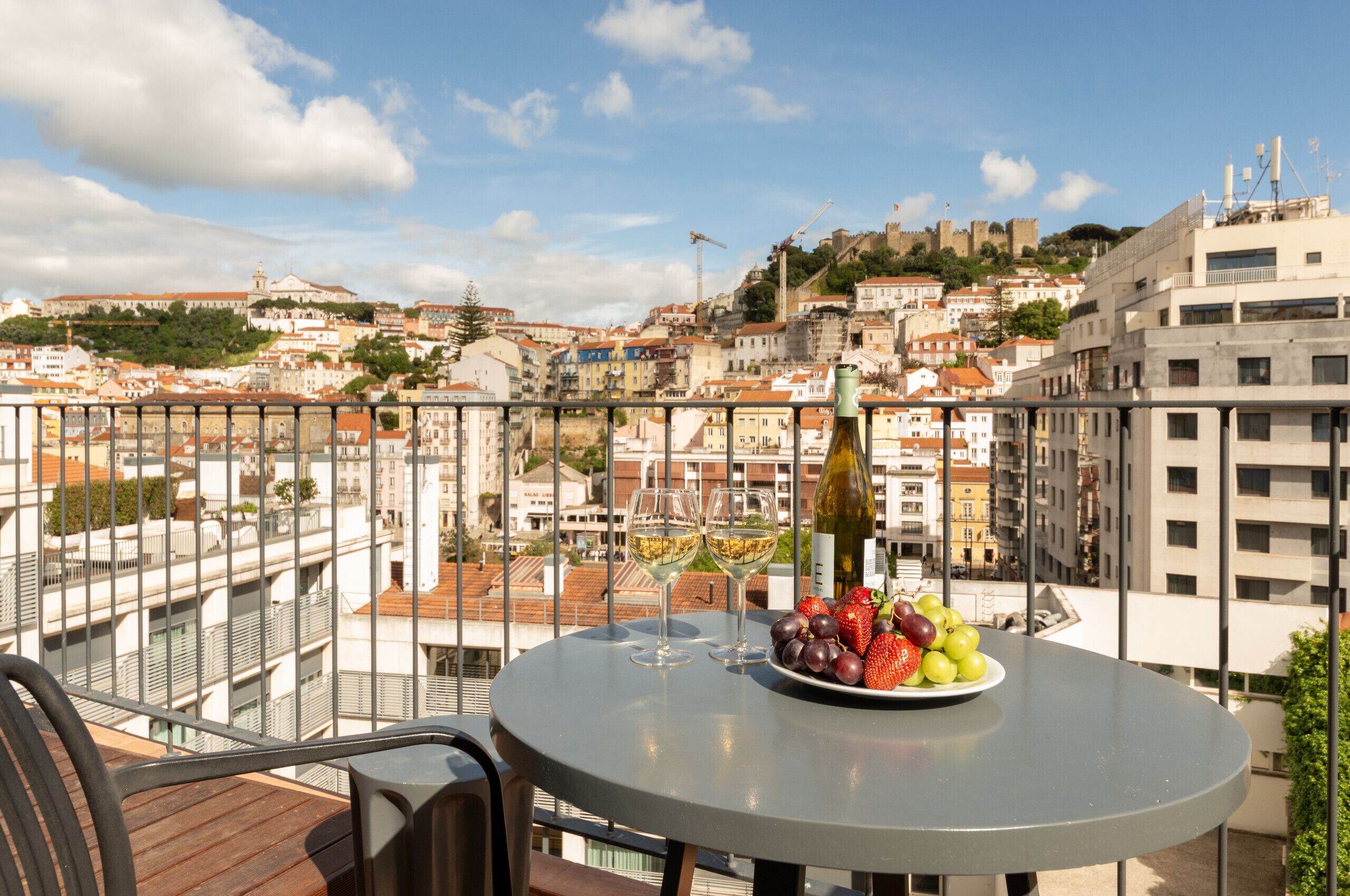 A balcony with a table, two wine glasses, and a plate of fruit.