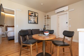 Un coin repas avec une table ronde en bois, quatre chaises, un saladier de fruits et des verres à vin.