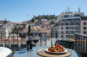 Un balcon avec une table dressée pour deux personnes, une bouteille de vin rouge et une assiette de fraises.