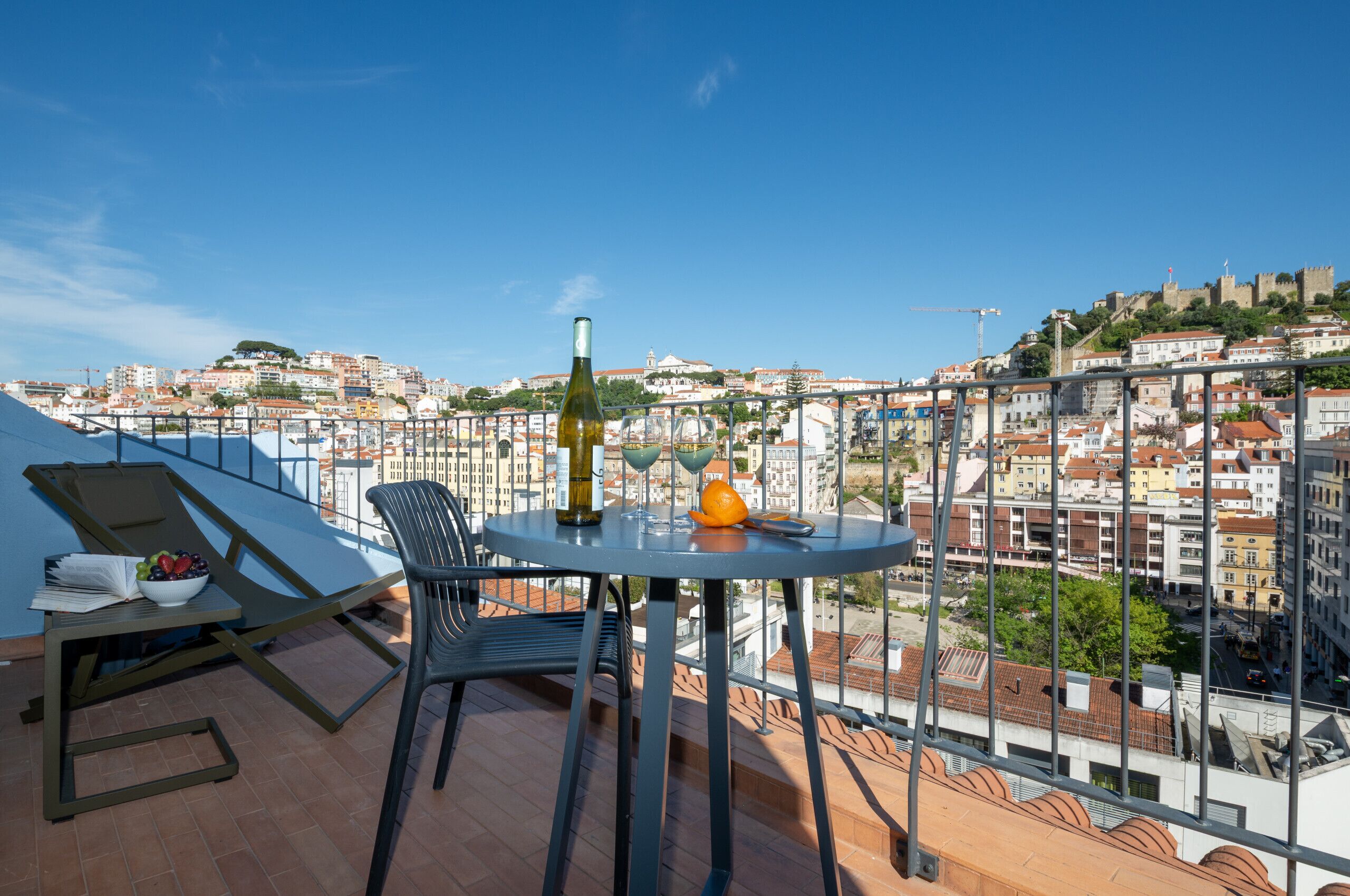 Un balcon avec une table, une bouteille et un saladier de fruits.