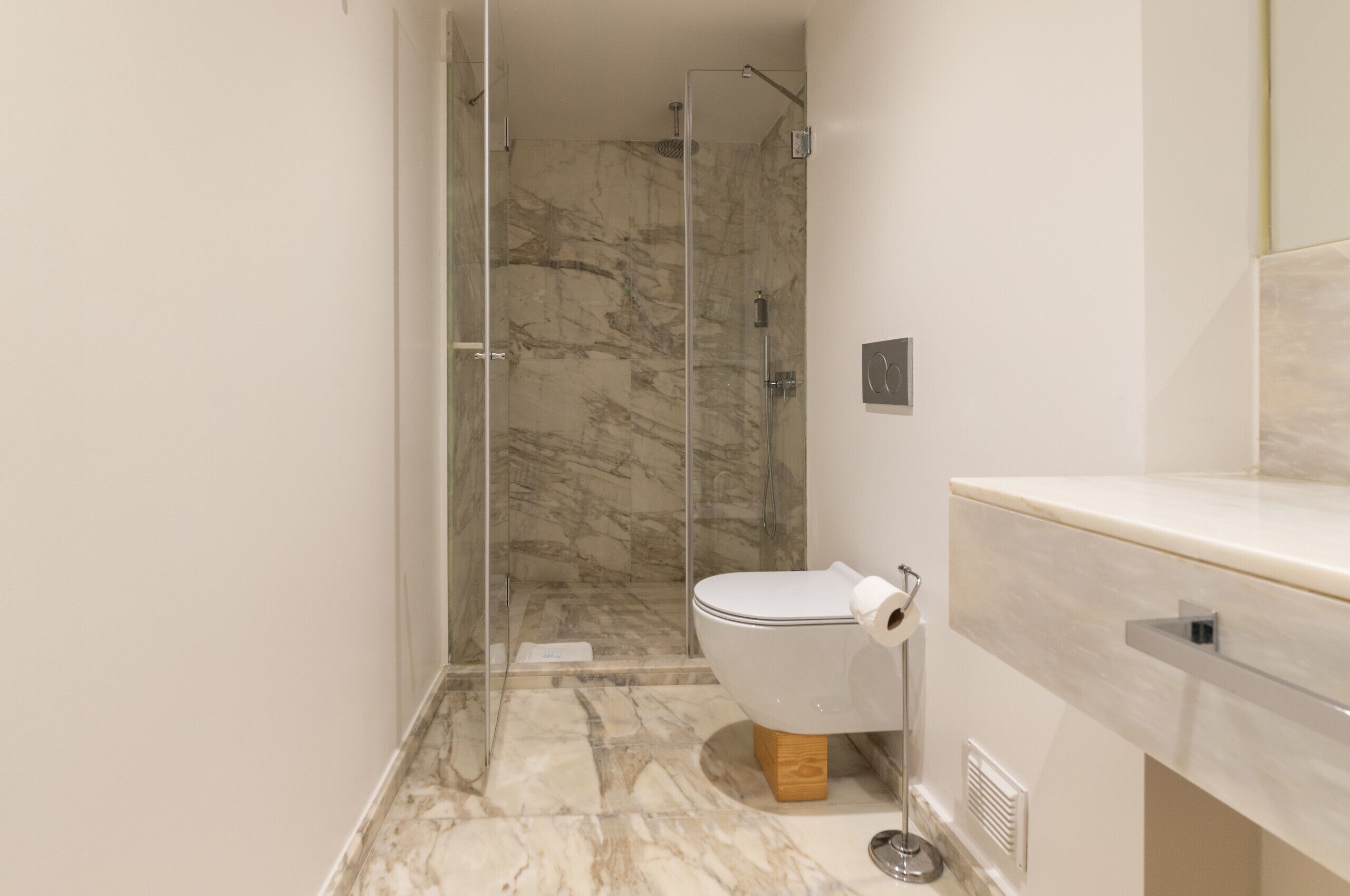 A modern bathroom with a glass-enclosed shower, a toilet with a marble floor, and a white sink.
