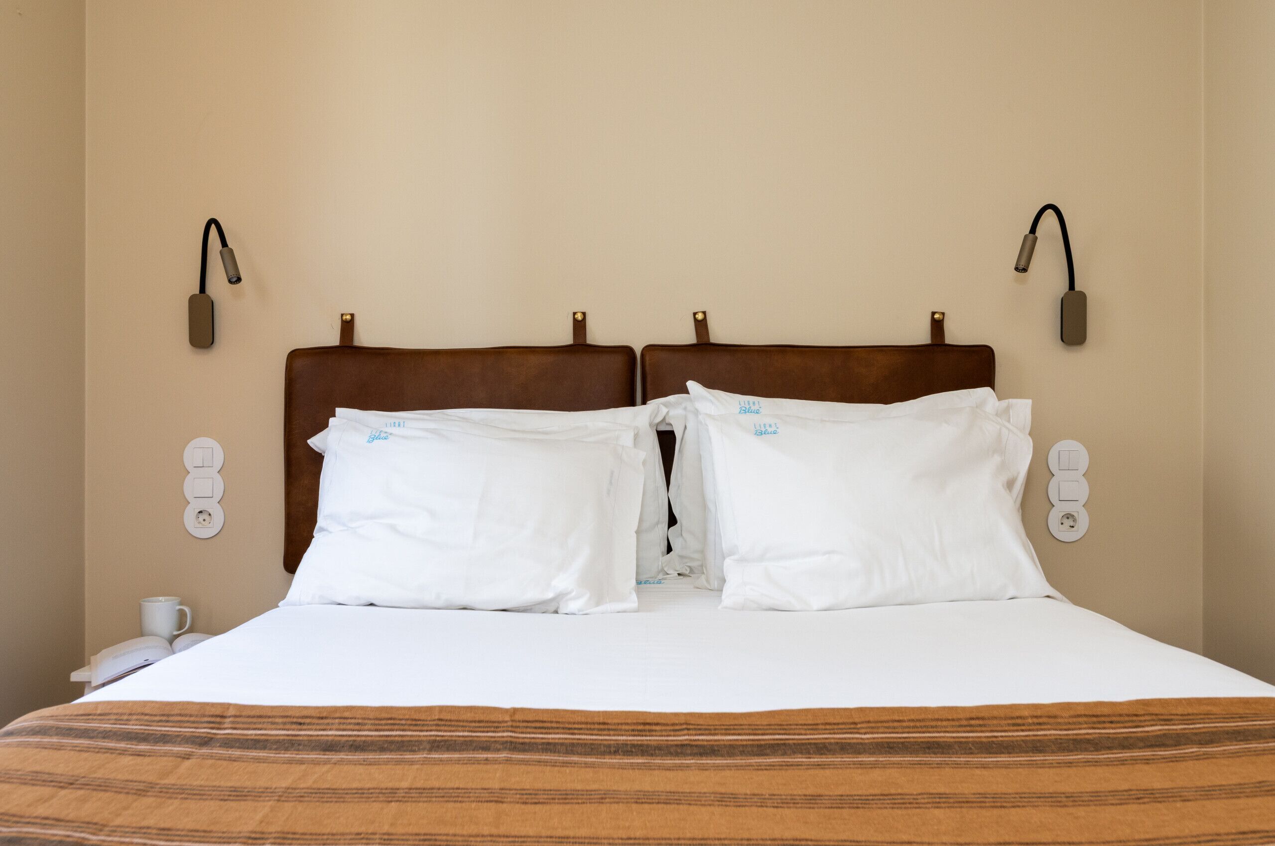 Una habitación de hotel con una cama grande, dos lámparas de noche, un teléfono junto a la cama y un enchufe en la pared.