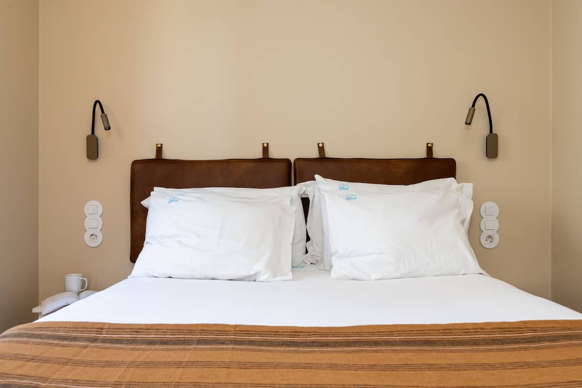 Une chambre d’hôtel avec un grand lit, deux lampes de chevet, un téléphone sur la table de chevet et une prise de courant au mur.