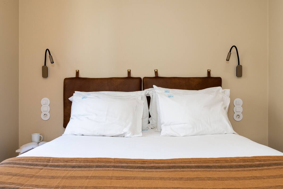 A hotel room with a large bed, two bedside lamps, a bedside phone, and a power outlet on the wall.