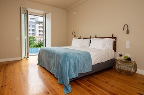 Ein Schlafzimmer mit einem Bett, einem Nachttisch mit einem Weinglas, einer Obstschale und Blick auf Gebäude durch eine Glastür.